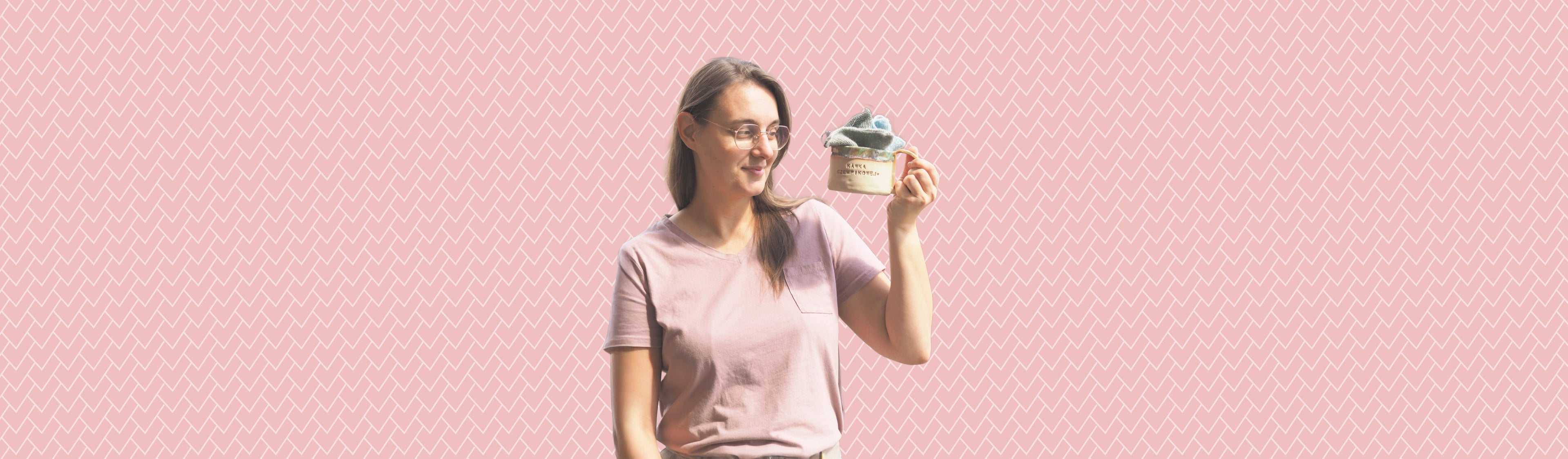 Dziewiarka na różowym tle trzymająca kubek wypełniony wełnianymi próbkami